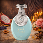 Türkisfarbener, ovaler Parfumflakon „Tahira“ von RIIFFS mit silbernem, kunstvoll verziertem Verschluss und rundem Ornament mit türkisfarbenem Stein in der Mitte. Der Flakon steht auf einer warm beleuchteten Oberfläche, umgeben von Mandeln, Vanilleschoten, Pralinenstücken, Rosenblüten und einer halbierten Drachenfrucht im Hintergrund.